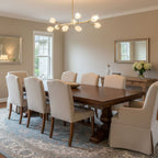 A branching Clérachic chandelier with white petal shades above a dark wood dining table and linen chairs, on a patterned blue rug.