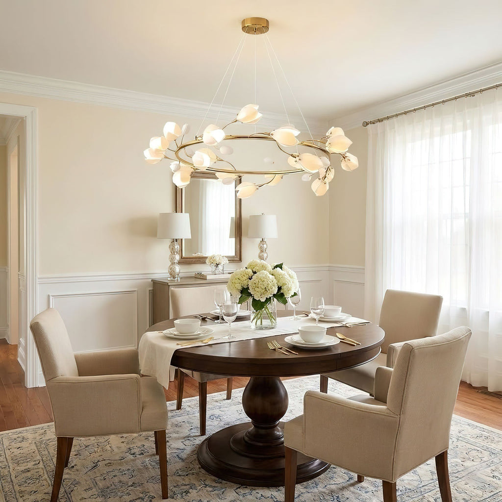 Gold ring Clérachic chandelier with white petals above a small round dining table set for tea, in a cream room with white curtains.