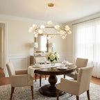 Gold ring Clérachic chandelier with white petals above a small round dining table set for tea, in a cream room with white curtains.