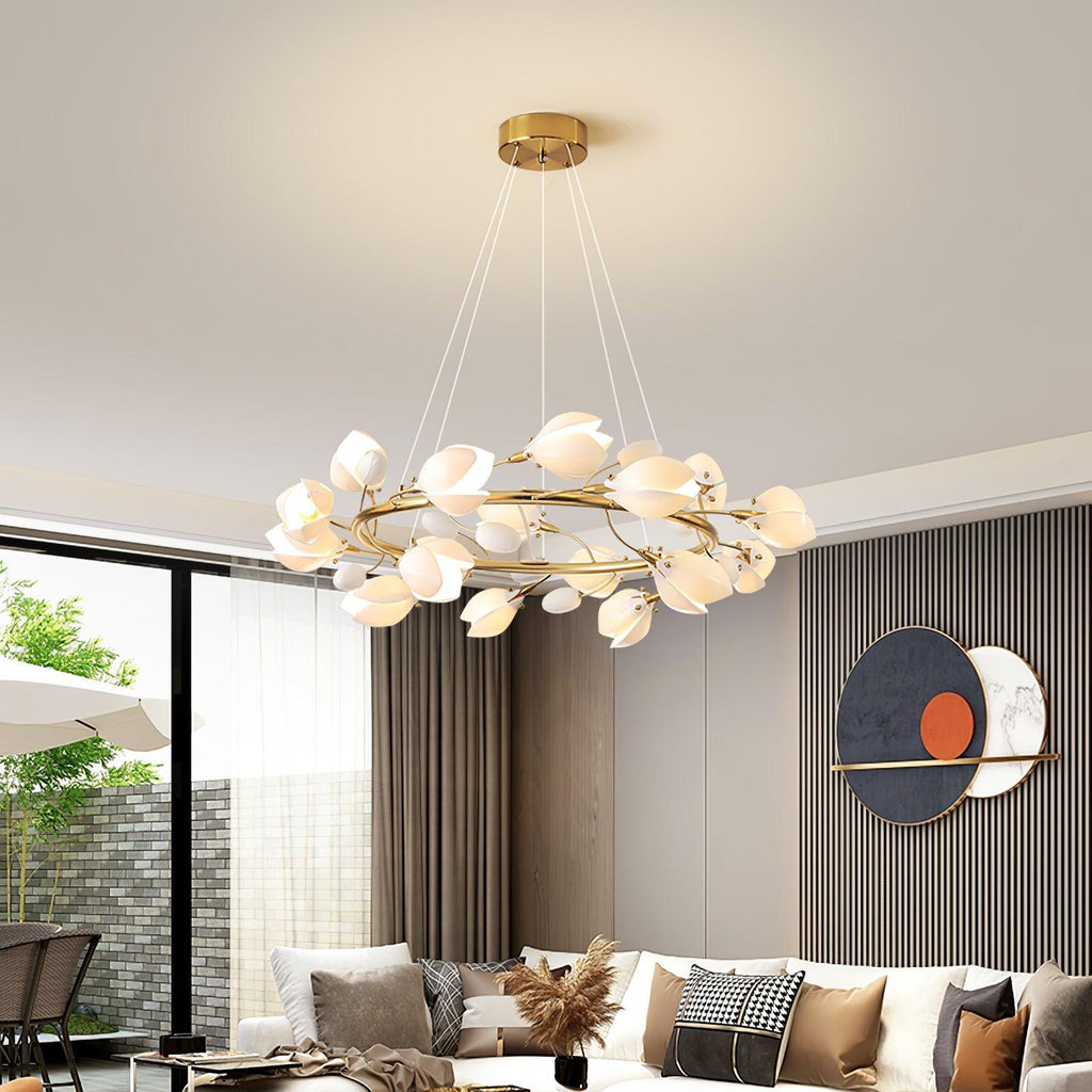 Lit Clérachic ring chandelier with white ceramic petals above a living room with a white sofa, slatted wall and a circular artwork.