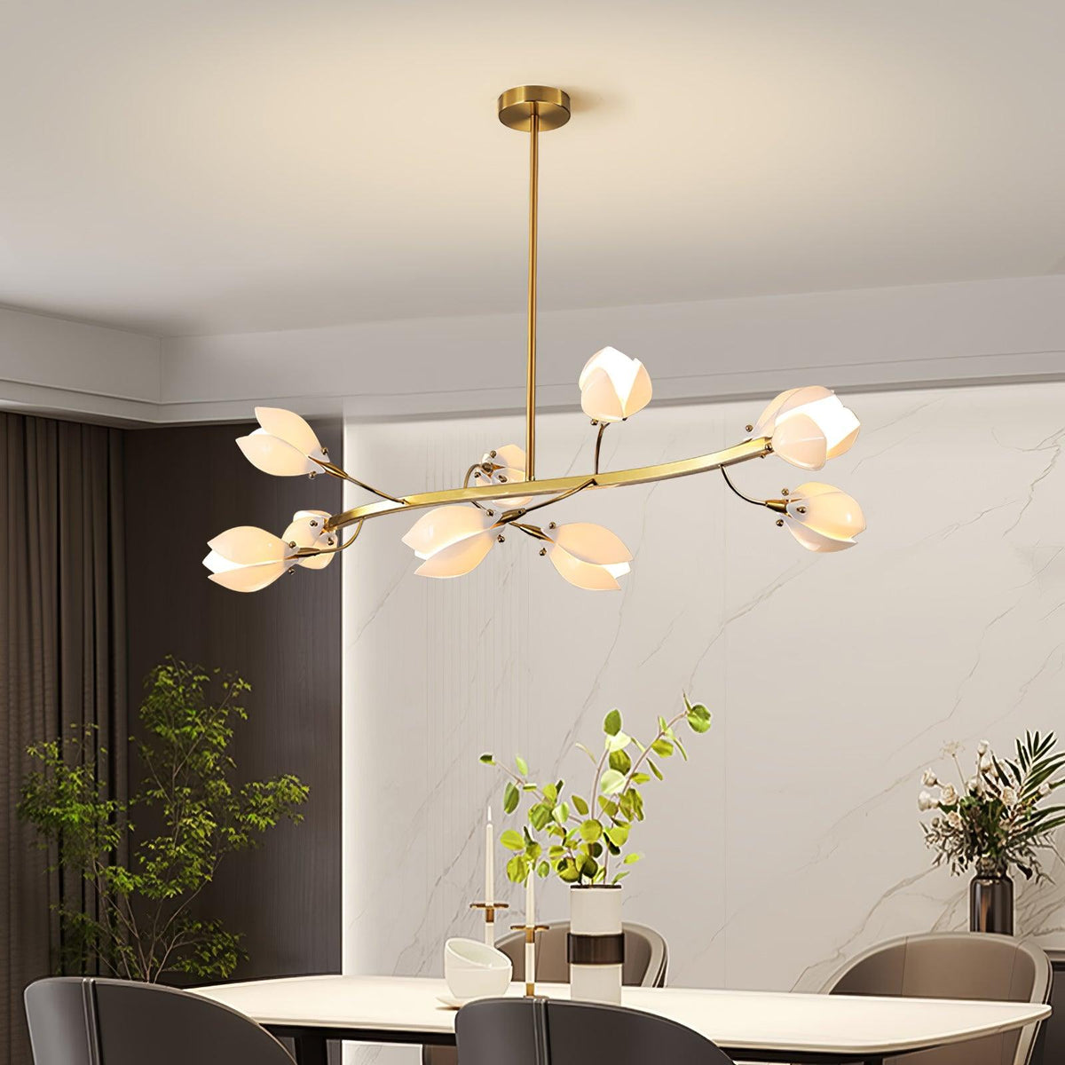 Clérachic petal chandelier on a straight gold rod, with a curved gold arm and white shades, above a dining table with grey chairs.