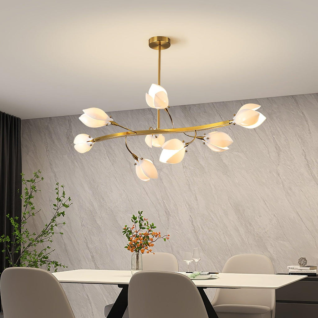 Clérachic chandelier with a wide curved gold arm and white petals, above a pale dining table in front of a grey stone-effect wall.