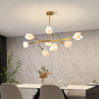 Clérachic chandelier with a wide curved gold arm and white petals, above a pale dining table in front of a grey stone-effect wall.