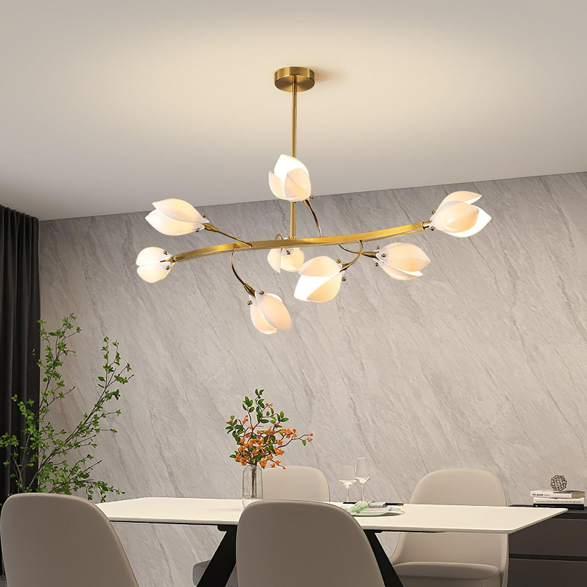 Clérachic chandelier with a wide curved gold arm and white petals, above a pale dining table in front of a grey stone-effect wall.