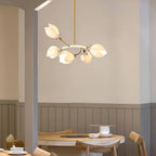 Lit Clérachic chandelier on a gold rod, with white petals on a curved gold arm, above a round wooden table by a panelled wall.