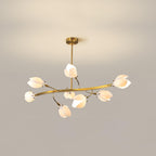 Clérachic chandelier with a gold rod, a long curved arm and white petal shades, lit against a plain beige wall.