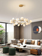 A Clérachic ring chandelier of white petals above a living room with a long white coffee table, green stools and a circular artwork.