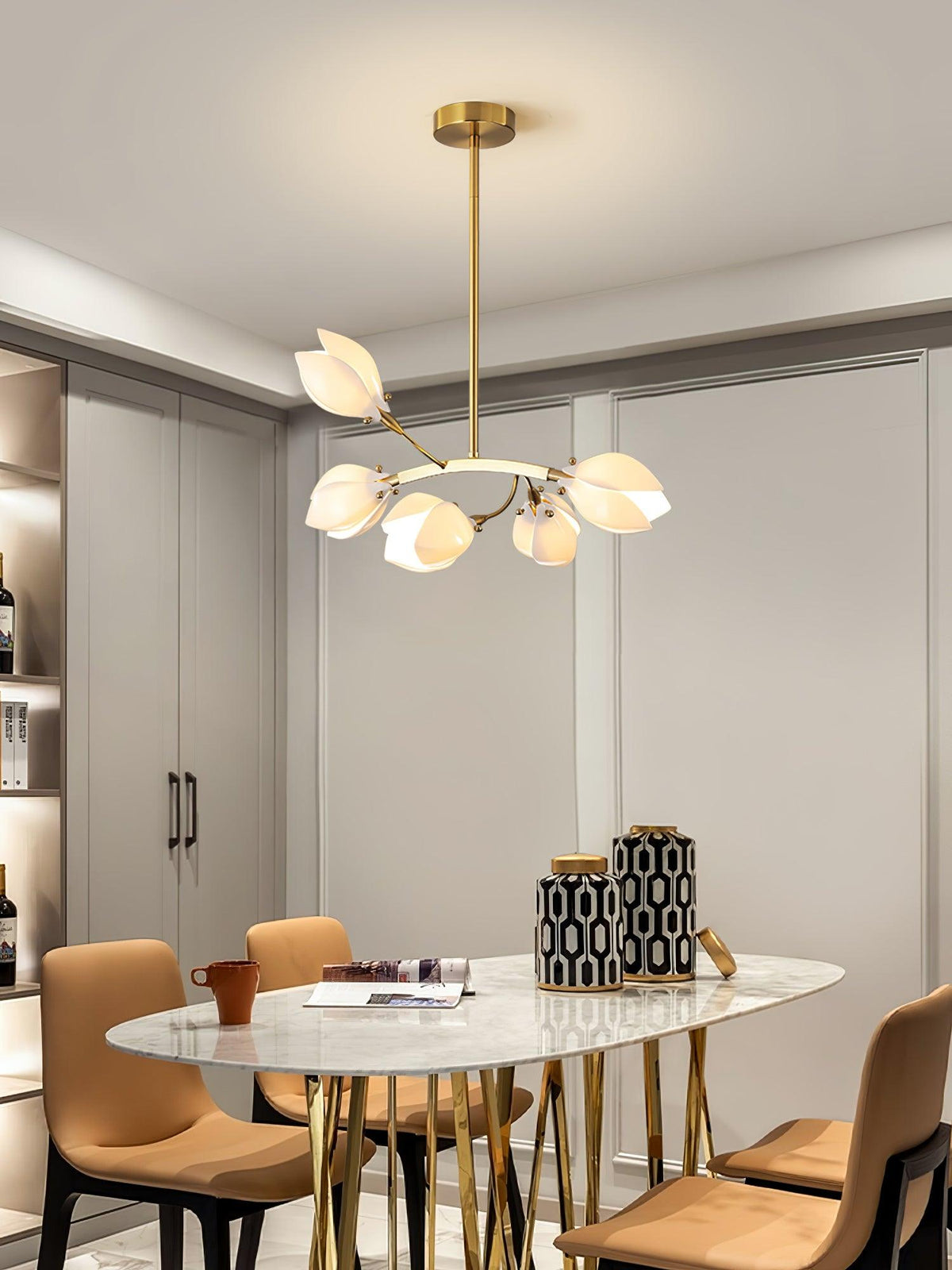 Clérachic petal chandelier on a gold rod above a marble-topped oval dining table with tan chairs and gold legs.