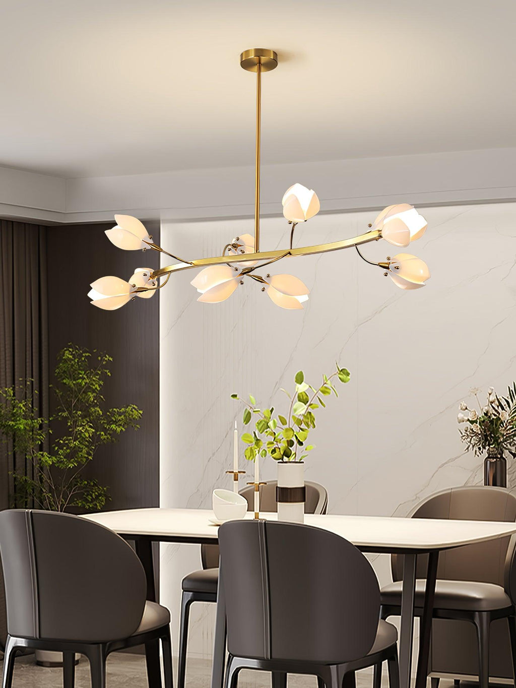 Lit Clérachic chandelier on a gold rod with curved arms of white petal shades, above a white dining table with dark grey chairs.