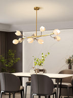 Lit Clérachic chandelier on a gold rod with curved arms of white petal shades, above a white dining table with dark grey chairs.