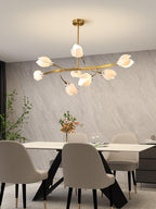 Clérachic chandelier with a long gold arm and white petals above a pale dining table and taupe chairs, against a grey stone-effect wall.