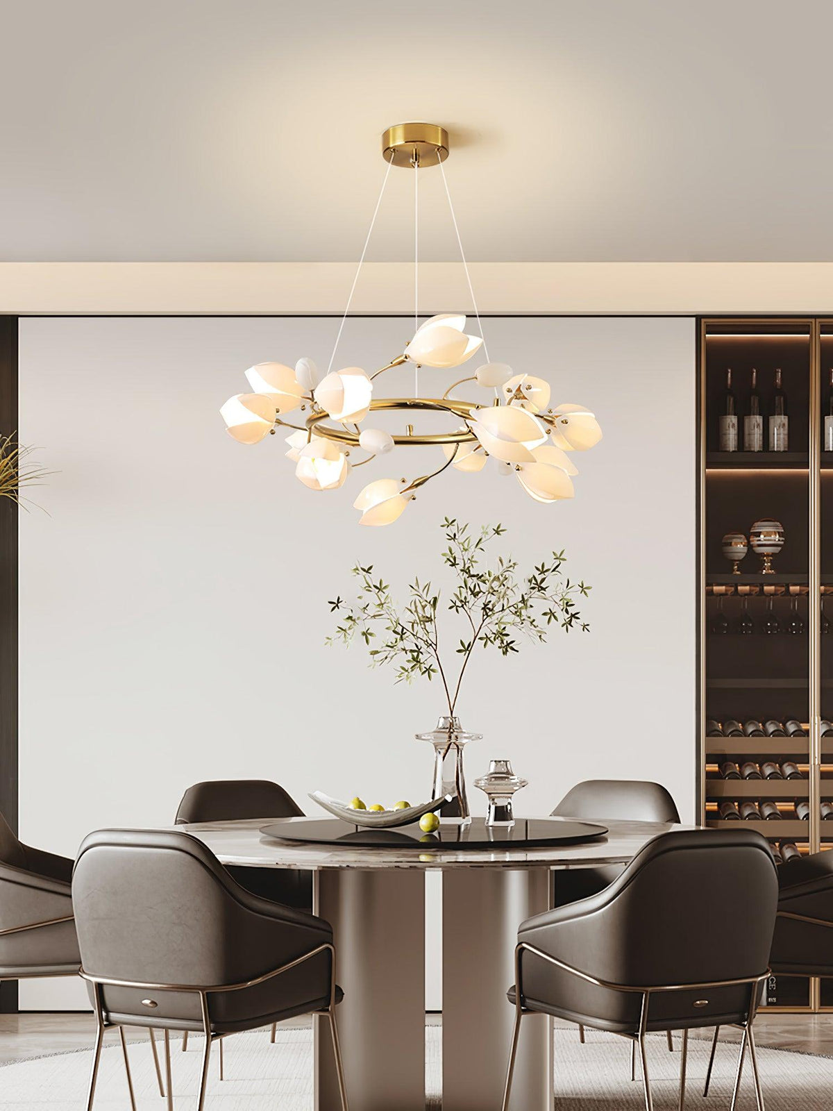 Clérachic ring chandelier lit above a round dining table with dark armchairs, in front of a pale wall and a wine display shelf.