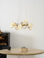 Lit Clérachic ring chandelier on white wall, hung above a round stone-topped table with a small candle holder and a black mug.