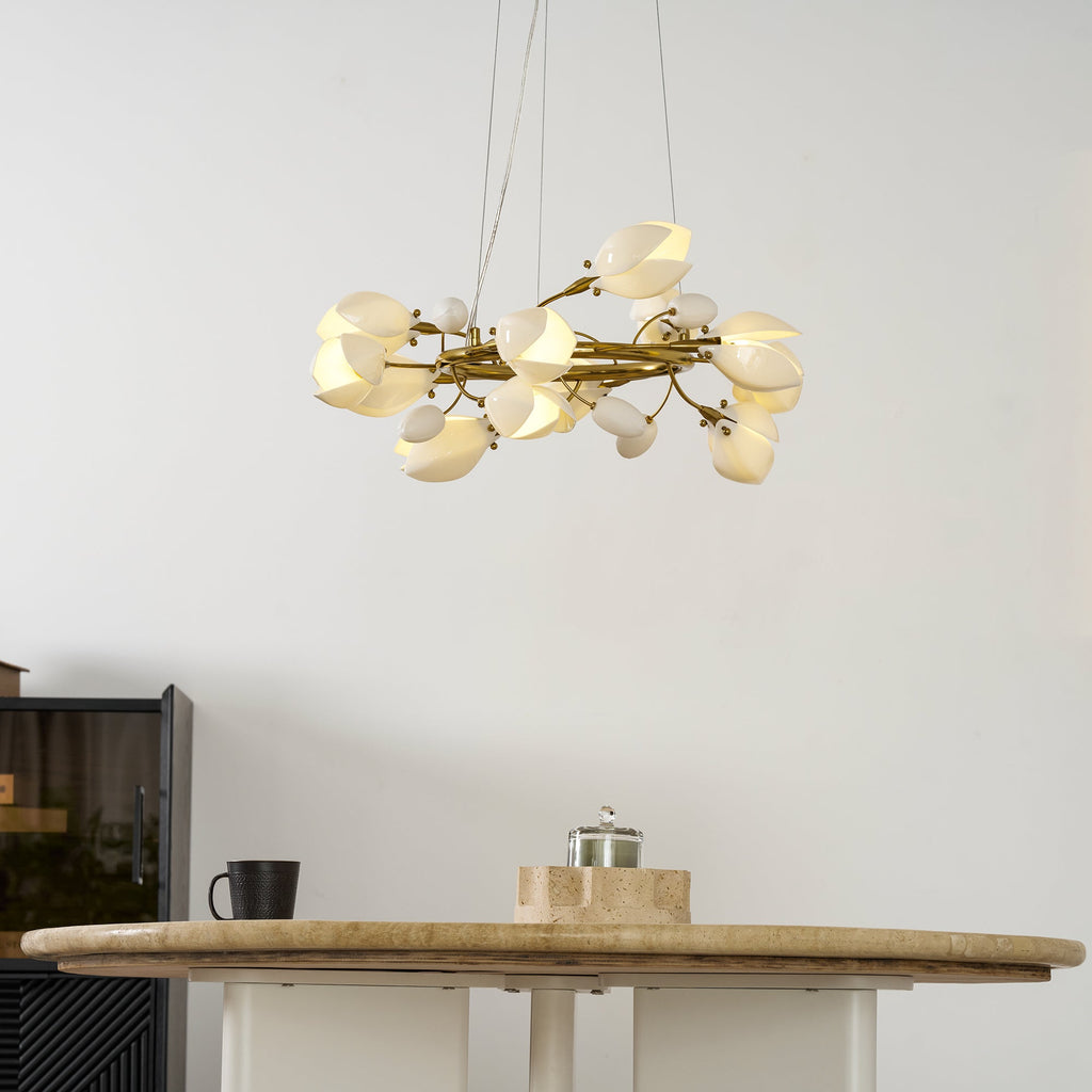 Side view of the lit Clérachic ring chandelier, with white petal shades along its gold ring, above the edge of a round stone-topped table.