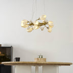 Side view of the lit Clérachic ring chandelier, with white petal shades along its gold ring, above the edge of a round stone-topped table.