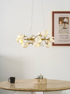 A Clérachic ring chandelier lit above a round travertine table, with a framed print on the wall and a black mug on the table.