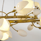 Close view of the gold ring, curved stems and white ceramic petal shades of this lit Clérachic chandelier, with small bud-shaped accents.