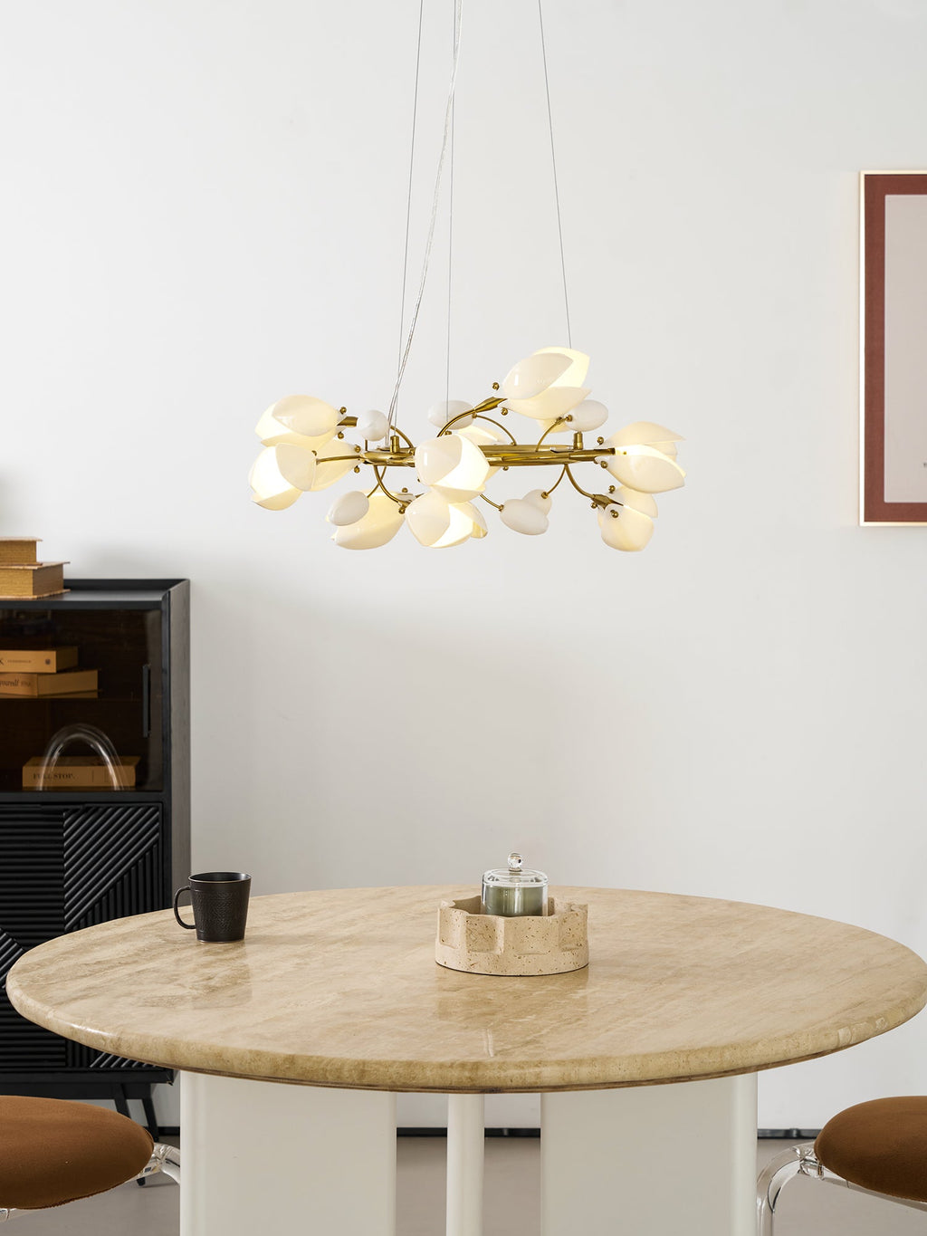 This Clérachic ring chandelier lit, centred above a round stone-topped table with a small candle holder, a mug and a framed print.