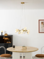 A wide view of the Clérachic ring chandelier on fine cables, hanging over a travertine table with brown stools and a framed print.
