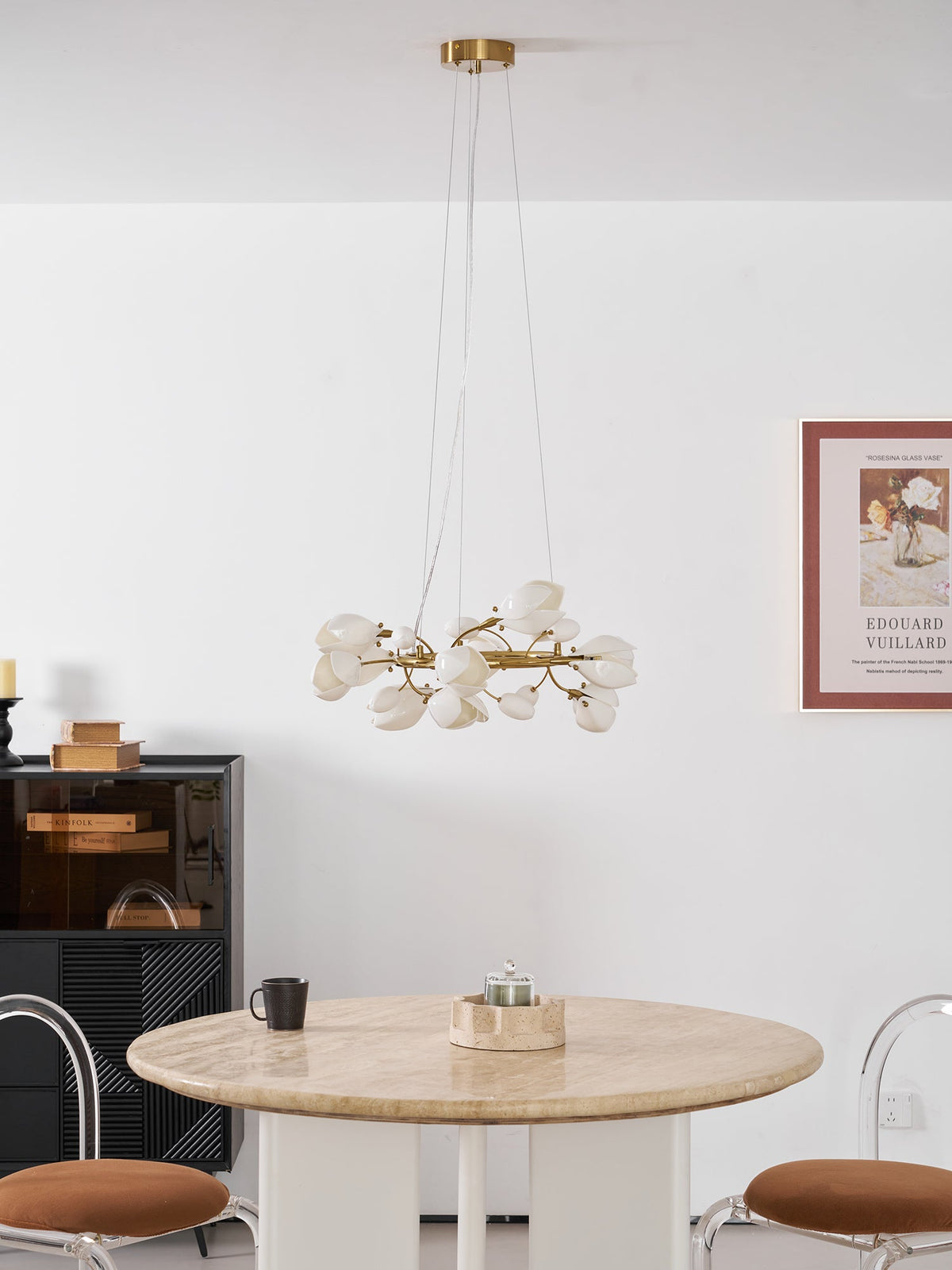 Clérachic ring chandelier on a gold canopy and cables, over a round stone table, with a black display cabinet and a framed print.
