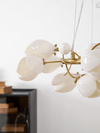 Close view of white ceramic petals, a gold ring and bud accents on this Clérachic chandelier, with a dark cabinet blurred behind.