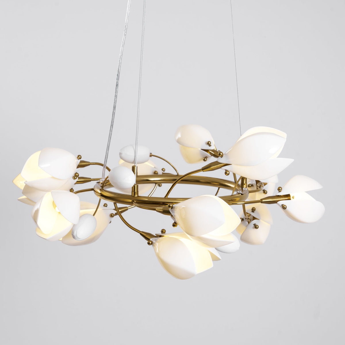 Clérachic chandelier lit on a grey backdrop, hung from two thin cables, with white petals and egg-shaped buds on a gold ring.