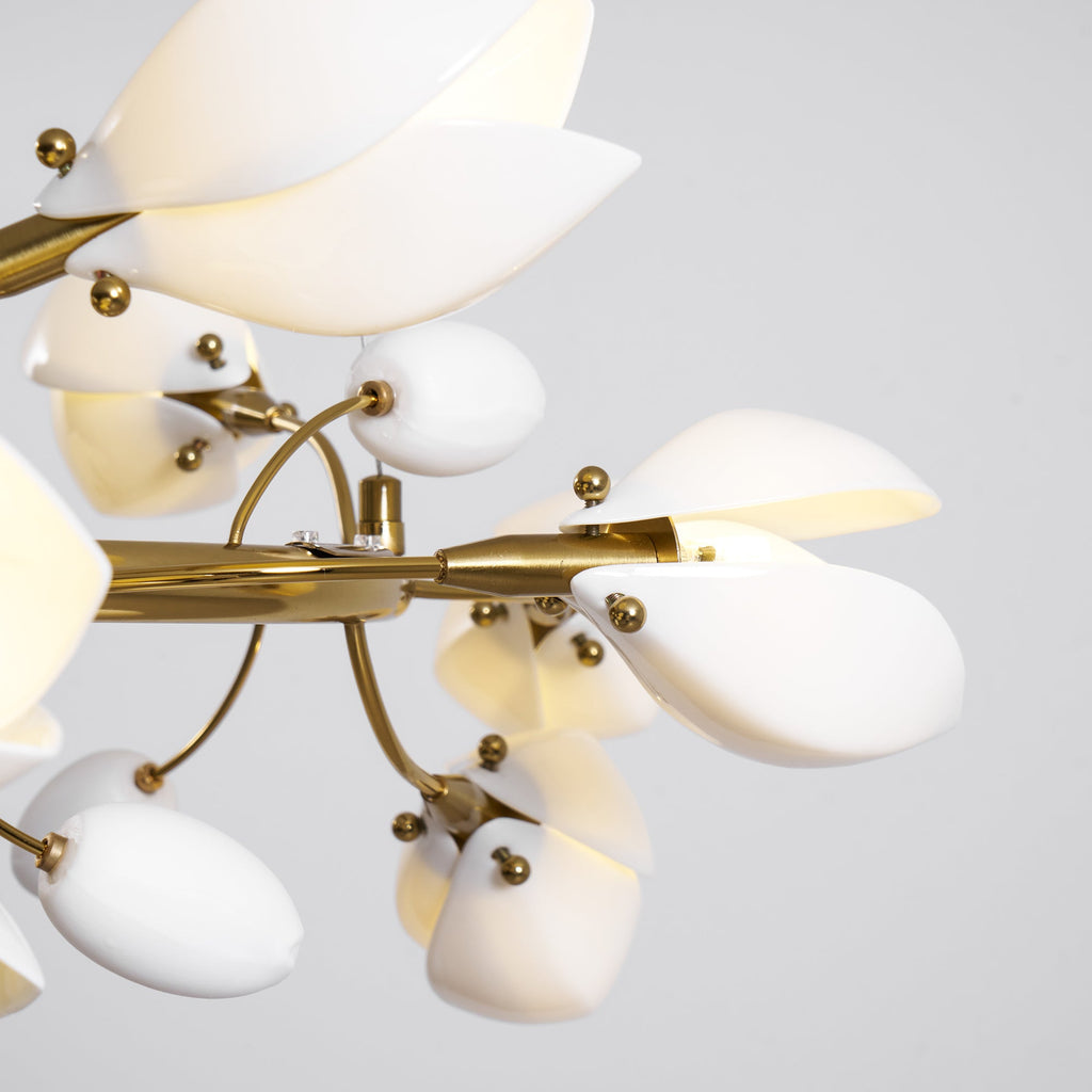 Close view of the gold ring, brass fittings and white ceramic petal and bud shades of this Clérachic chandelier on a grey backdrop.