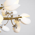 Close view of the gold ring, brass fittings and white ceramic petal and bud shades of this Clérachic chandelier on a grey backdrop.