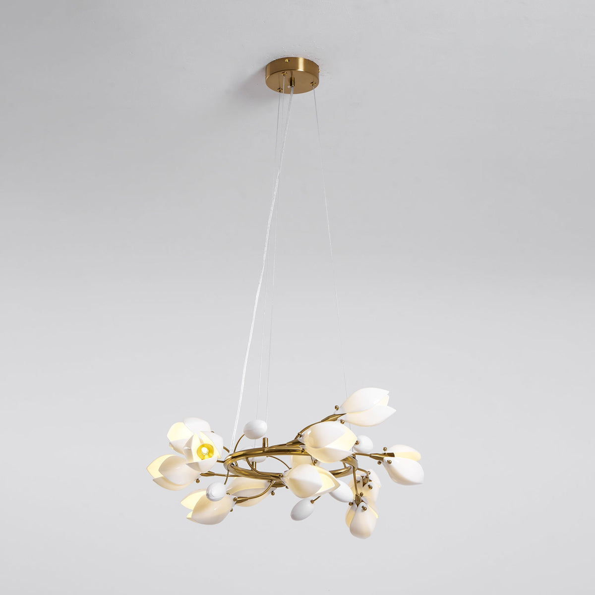 Clérachic ring chandelier hanging from a round gold canopy on fine cables, with one bulb lit among the white petal shades.