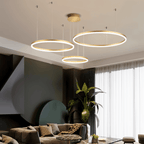 This Clérachic gold ring chandelier stacks three loops above a living room with a blush pink wall.