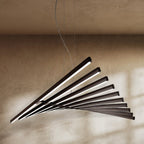 Clérachic's black bar chandelier fans in a sweeping curve, its LED bars glowing against a warm plaster wall.