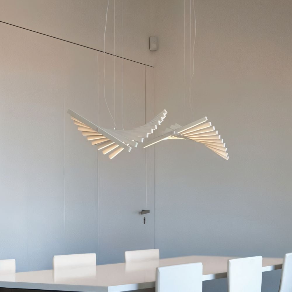 Clérachic's white bar chandelier curves above a dining table, its fanned bars glowing warm in a bright room.