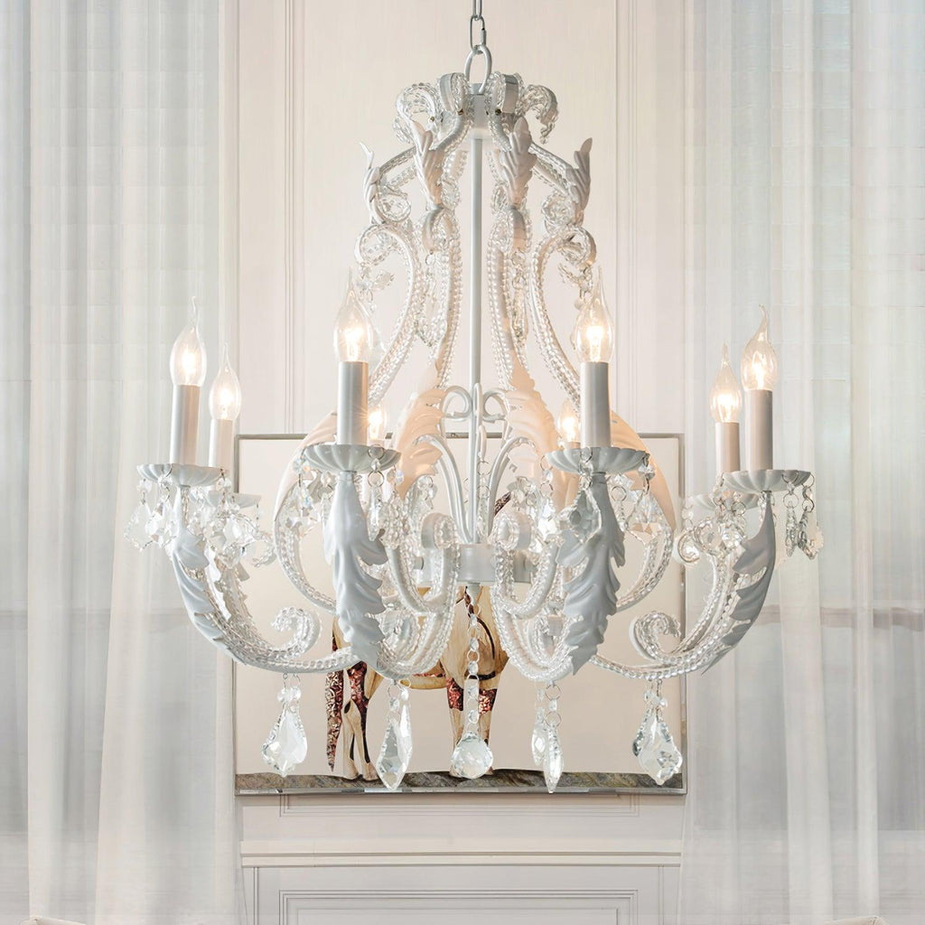Hung before sheer curtains, this Clérachic chandelier shows curling white scrollwork, crystal drops and candle-style lights.