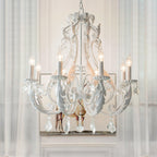 Hung before sheer curtains, this Clérachic chandelier shows curling white scrollwork, crystal drops and candle-style lights.