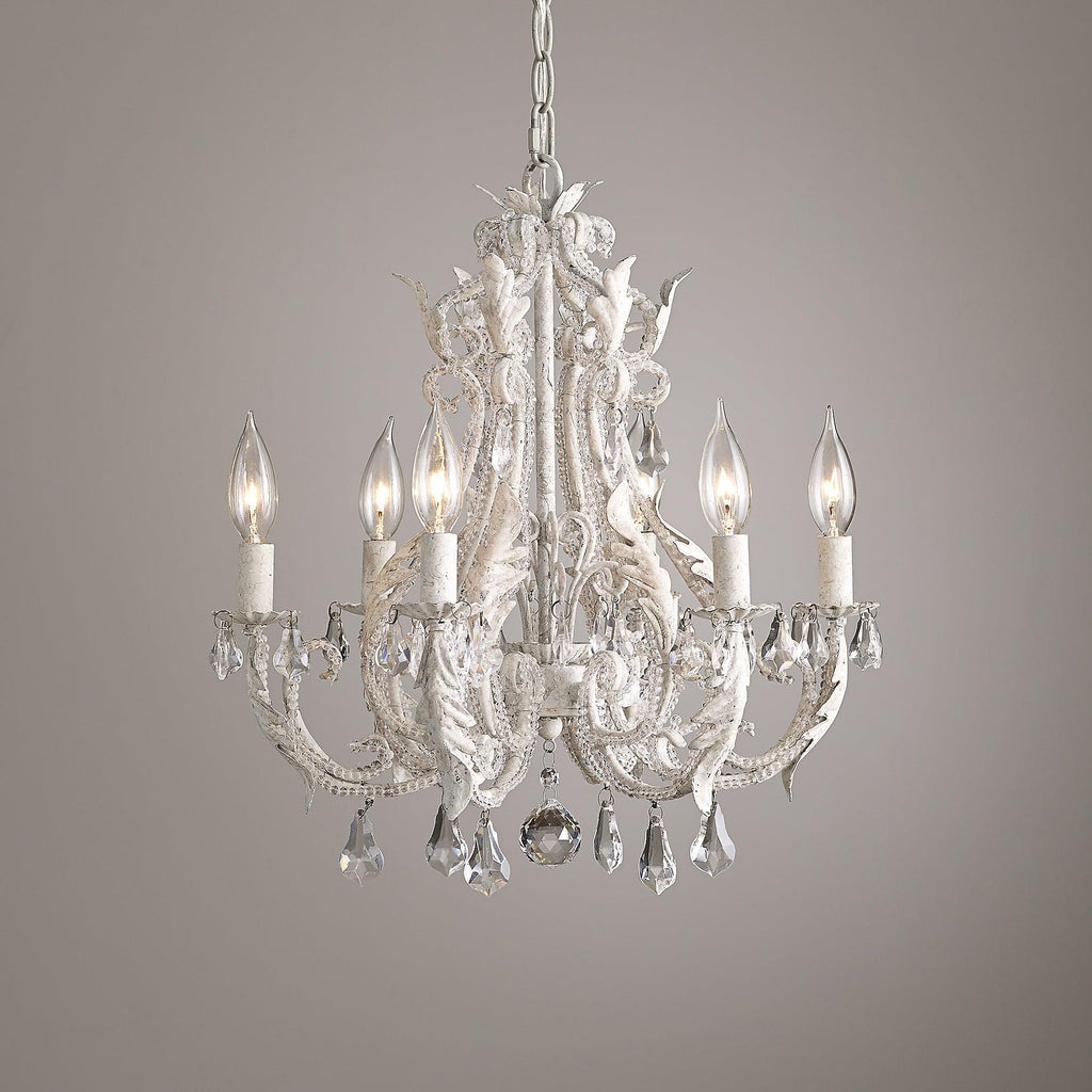 A Clérachic chandelier with white scrolling arms and clear crystal pendants, photographed against a soft mauve-grey wall.