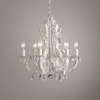 A Clérachic chandelier with white scrolling arms and clear crystal pendants, photographed against a soft mauve-grey wall.