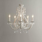 Straight-on view of a Clérachic chandelier with unlit candle sleeves, beaded scrollwork and crystal drops on a grey backdrop.