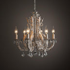 A Clérachic chandelier lit against a dark brown backdrop, with warm candle bulbs glowing behind its crystal drops.
