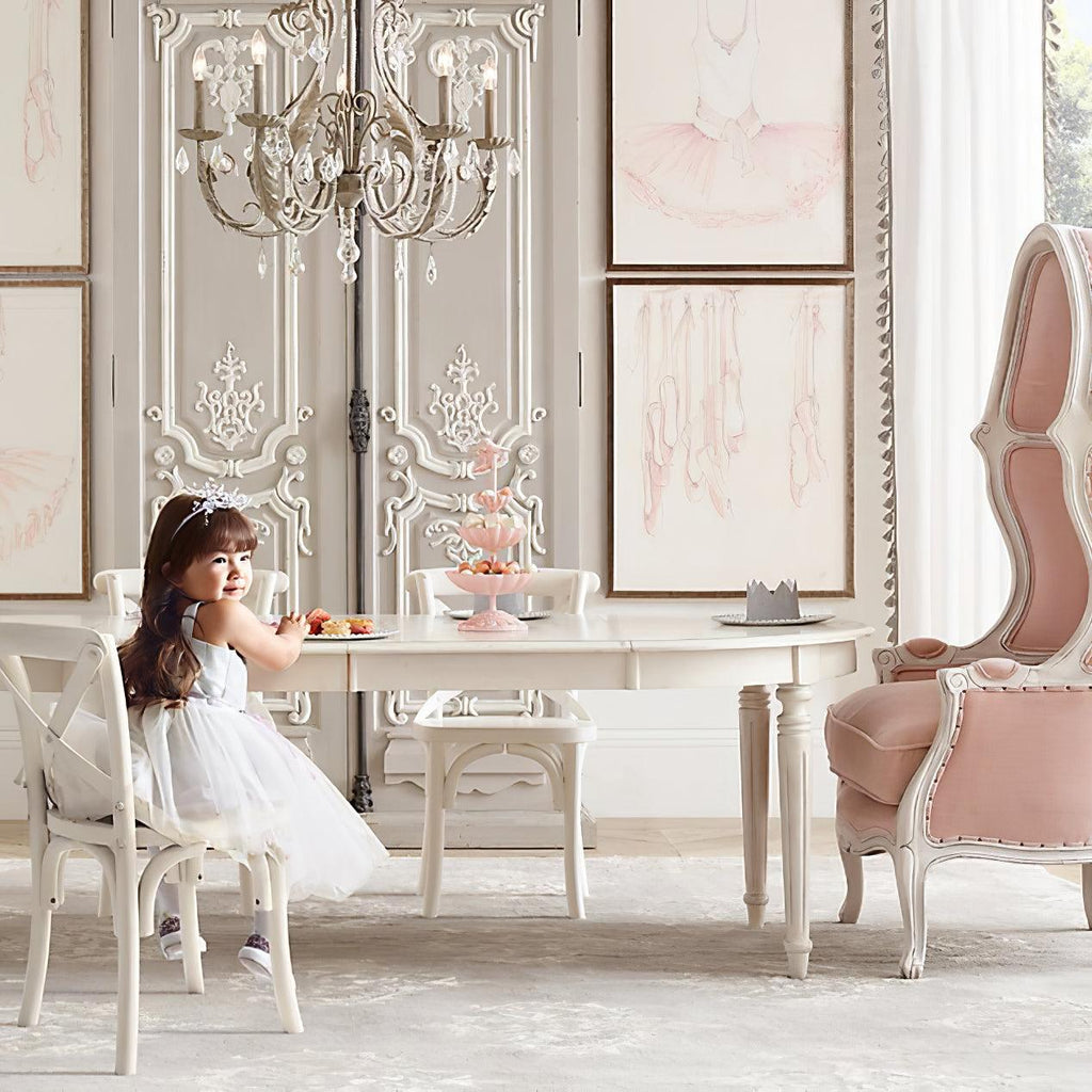 A Clérachic chandelier hangs above a girl at a small white table, in a room with carved white panelling and a pink armchair.