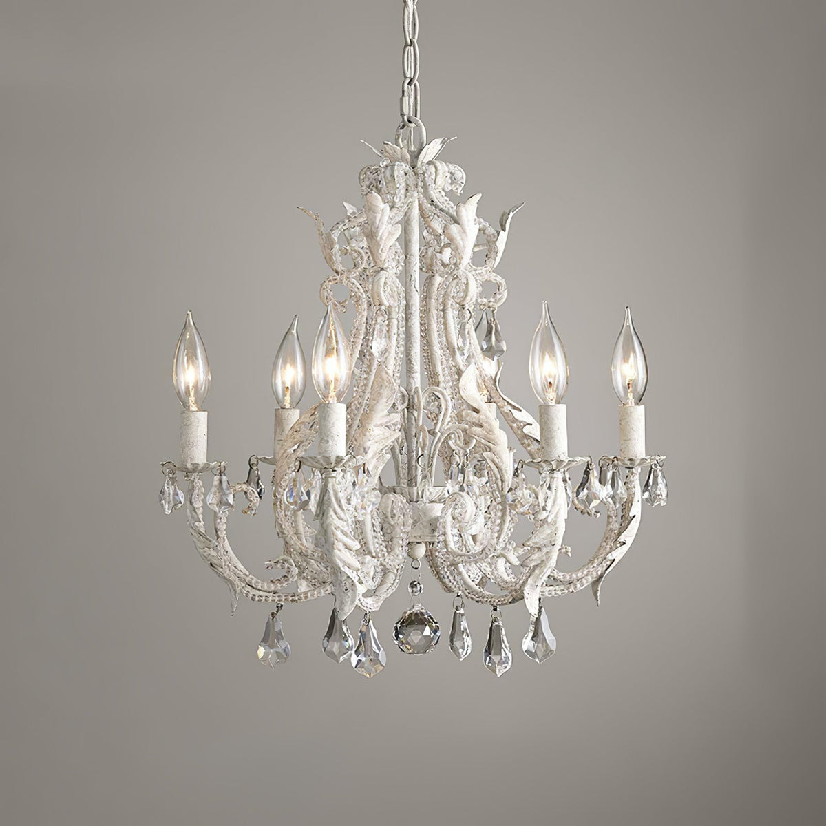 A Clérachic chandelier with ivory candle sleeves and a large centre crystal ball, photographed against a grey wall.