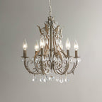 A Clérachic chandelier in an aged taupe-brown version with clear crystal drops, lit with candle bulbs against a grey wall.