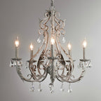 A Clérachic chandelier with a wider arm spread, antique-white scrollwork and clear crystal drops, against a grey wall.
