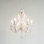 A white Clérachic chandelier with five lit candle bulbs and crystal drops, photographed against a light grey backdrop.