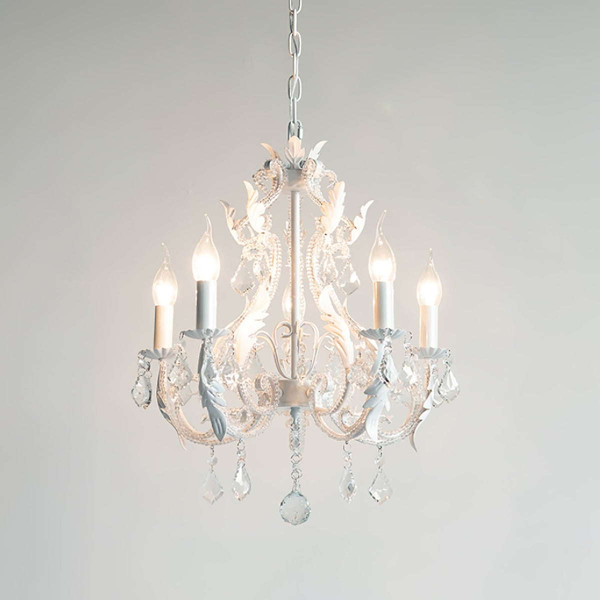 A white Clérachic chandelier with five lit candle bulbs and crystal drops, photographed against a light grey backdrop.