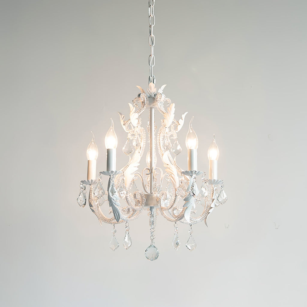 A Clérachic chandelier glowing softly against a pale grey backdrop, with white scrolled arms and clear crystals.