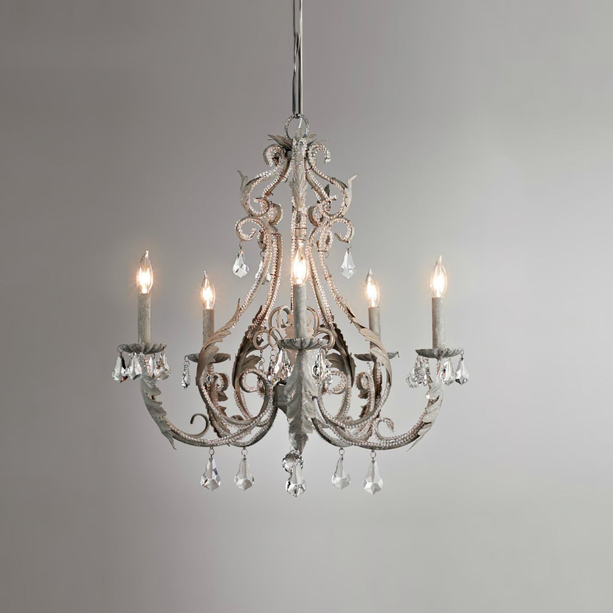 A Clérachic chandelier in an aged grey-white finish, with unlit candle sleeves, on a grey gradient backdrop.
