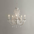 A Clérachic chandelier with unlit candle sleeves, beaded white scrollwork and crystal drops, against a mid-grey wall.