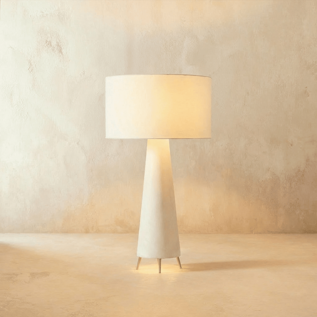 Clérachic white fabric drum shade glowing warm over a tapering cream base on three slim metal feet, against limewash.