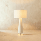 Clérachic white fabric drum shade glowing warm over a tapering cream base on three slim metal feet, against limewash.