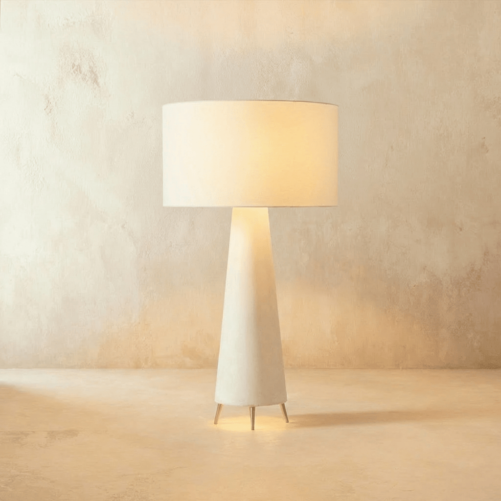 Clérachic mid-size white drum shade glowing warm over a tapering cream base on three pointed metal feet.